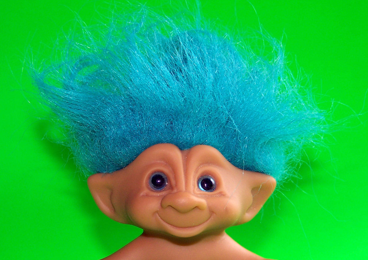 Front view of vintage troll doll head showcasing bright blue frizzy hair on green background