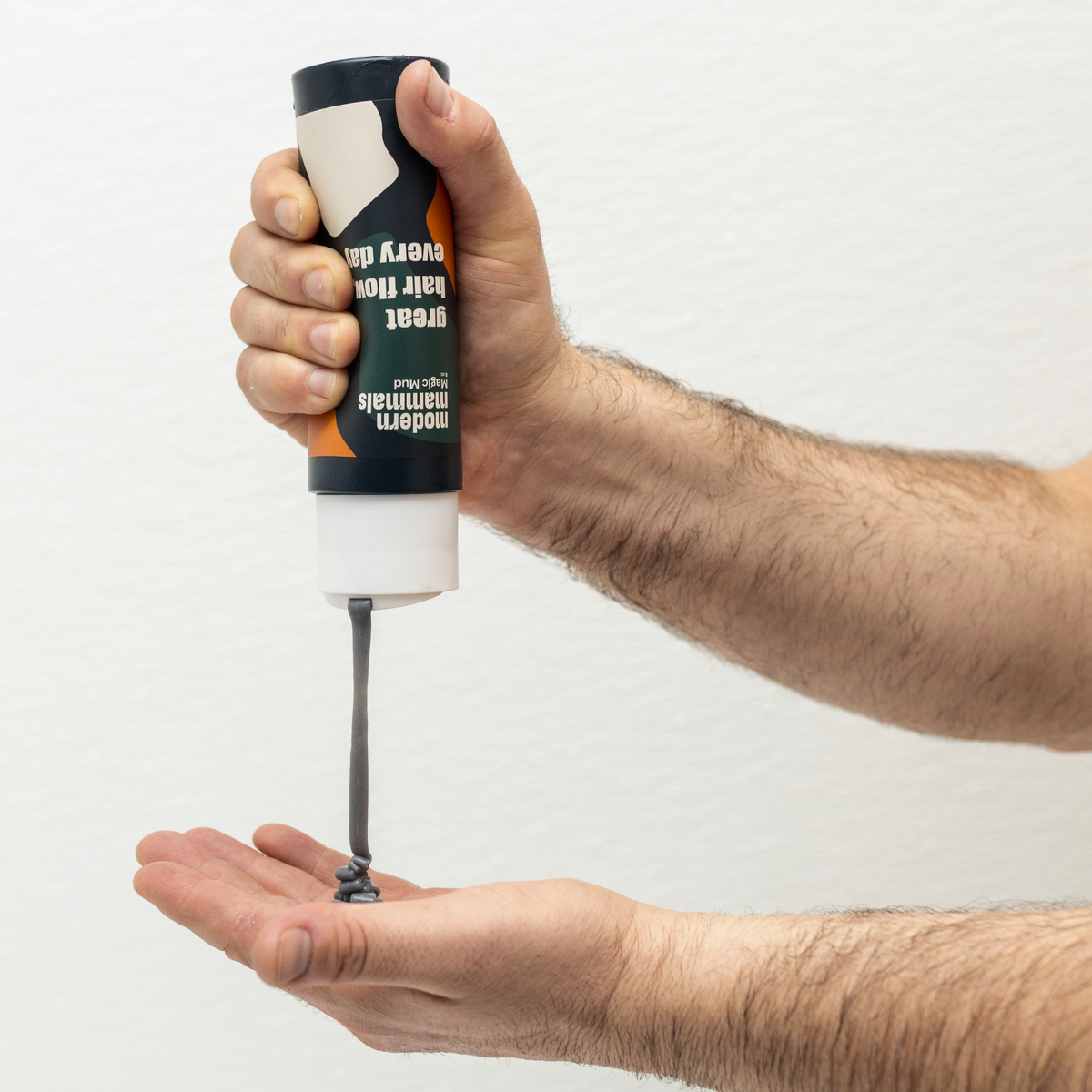 Hand squeezing Modern Mammals Magic Mud hair wash into another palm, thick charcoal-gray paste on white background