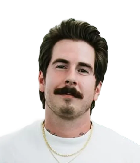 Smiling barber head-and-shoulders portrait with dark hair, mustache, white shirt and gold chain