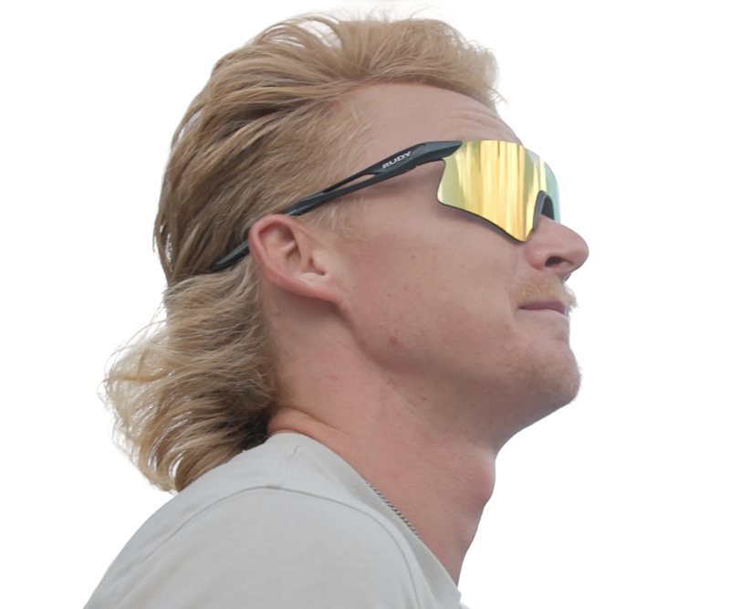 Man with blonde mullet and reflective sports sunglasses looking upward in profile