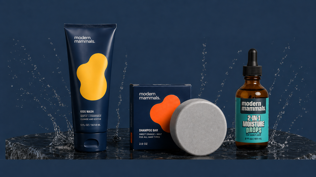 Front view of three products on a navy backdrop with water splashes: Kids Wash, shampoo bar, 2-in-1 Moisture Drops