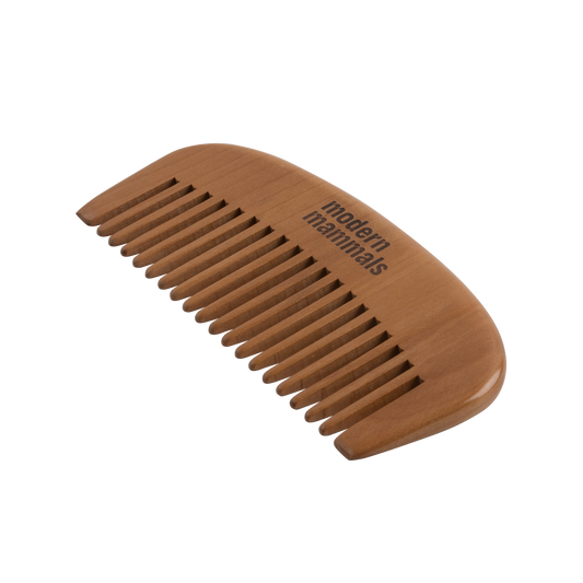 Angled top-down view of wide-tooth wooden comb showcasing smooth wide teeth and Modern Mammals engraving on a white background
